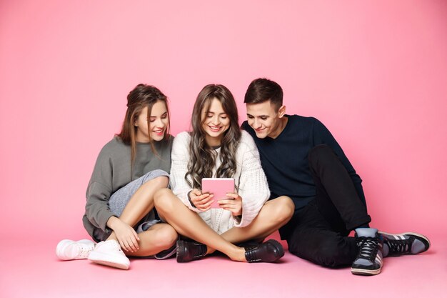 Young friends smiling looking at tablet on pink