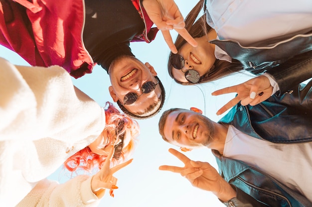 Free photo young friends standing in circle and showing peace gesture