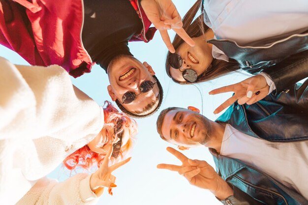 Young friends standing in circle and showing peace gesture