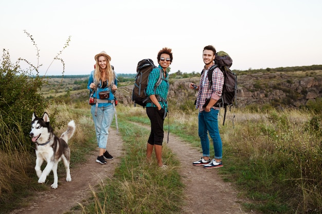 Юные друзья с рюкзаками и хаски улыбаются, путешествуя по каньону