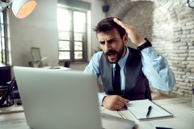 Бесплатное фото Молодой разочарованный бизнесмен спорит с кем-то во время онлайн-встречи за компьютером в офисе