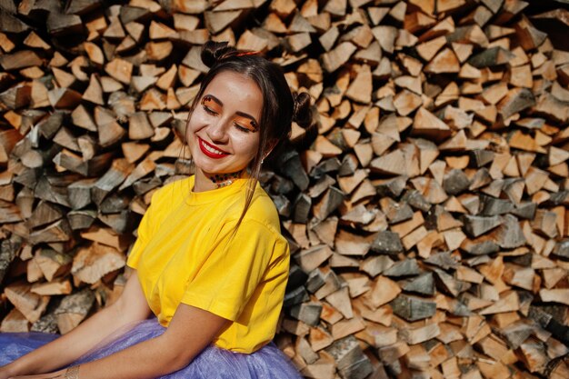 Young funny girl with bright makeup like fairytale princess wear on yellow shirt and violet skirt against wooden background