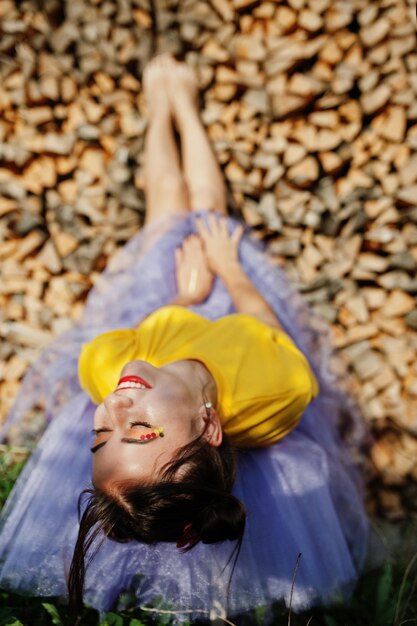 Young funny girl with bright makeup like fairytale princess wear on yellow shirt and violet skirt lying against wooden background