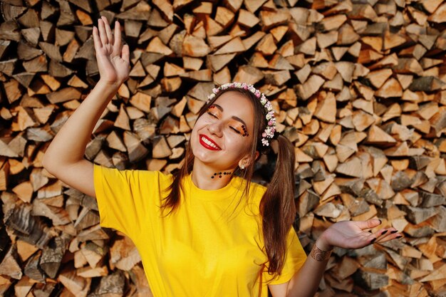 Young funny girl with bright makeup wear on yellow shirt and wreath against wooden background