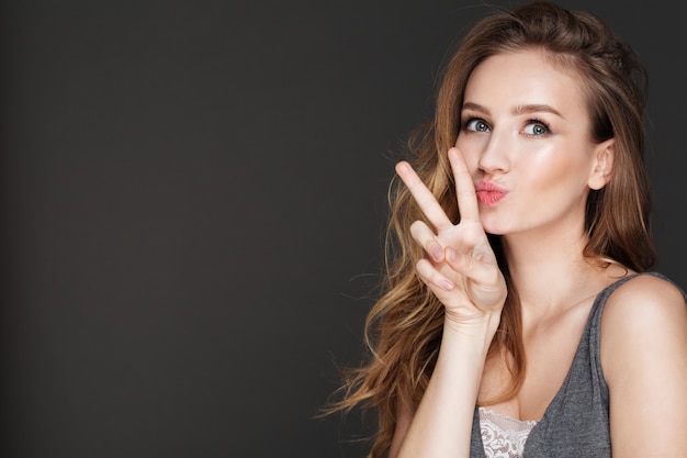 Young funny lady posing while make peace gesture.