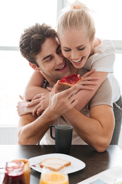 Young funny man feed his lady with bread and jam while have breakfast