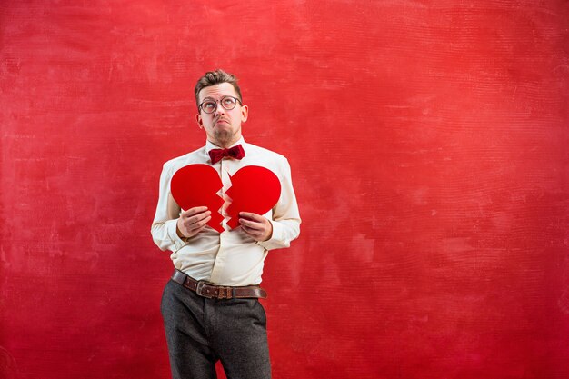 The young funny man with abstract broken heart on red studio background. Concept - unhappy love