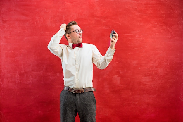 young funny man with abstract clock on red studio background.