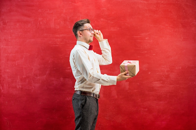 Young funny man with gift on red studio background