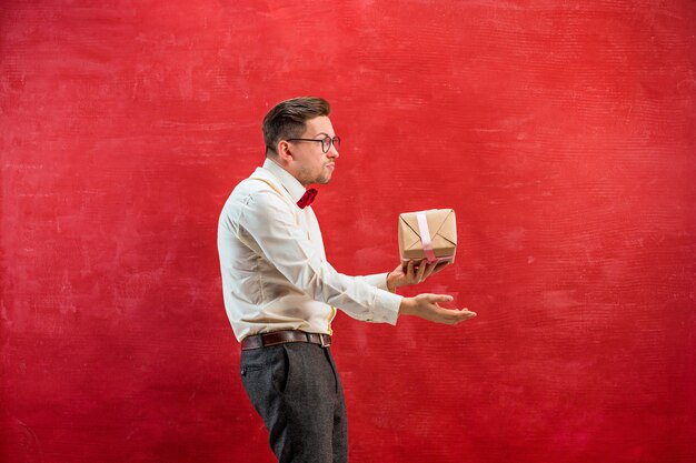 Young funny man with gift on red studio background