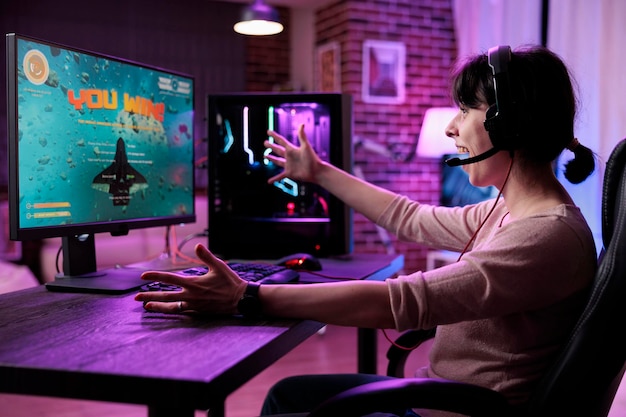Young gamer celebrating video games championship win on online live stream, feeling happy at desk with neon lights. Female streamer winning shooter gaming tournament on computer.