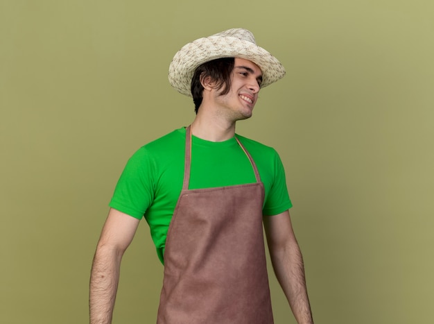 Free photo young gardener man in apron and hat looking aside with smile on face happy and positive standing over light background