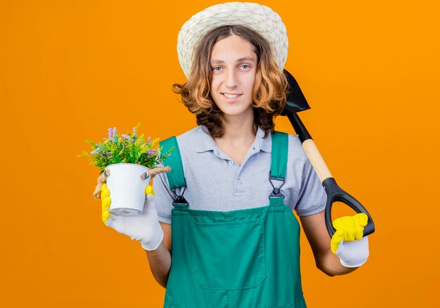 Free photo young gardener man in rubber gloves wearing jumpsuit and hat holding shovel