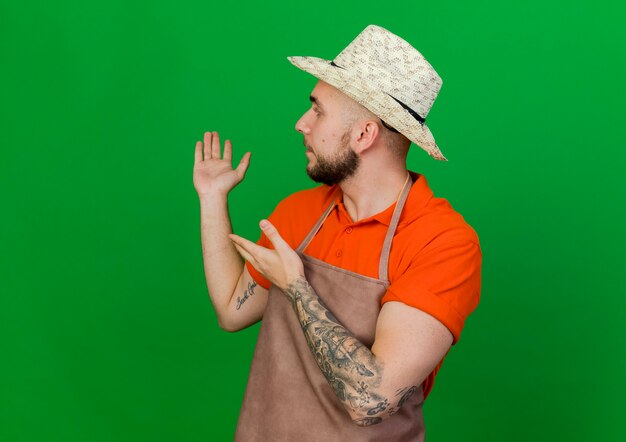 Free photo young gardener man wearing gardening hat looks and points behind