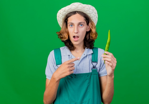 緑の唐辛子を指しているジャンプスーツと帽子をかぶっている若い庭師の男