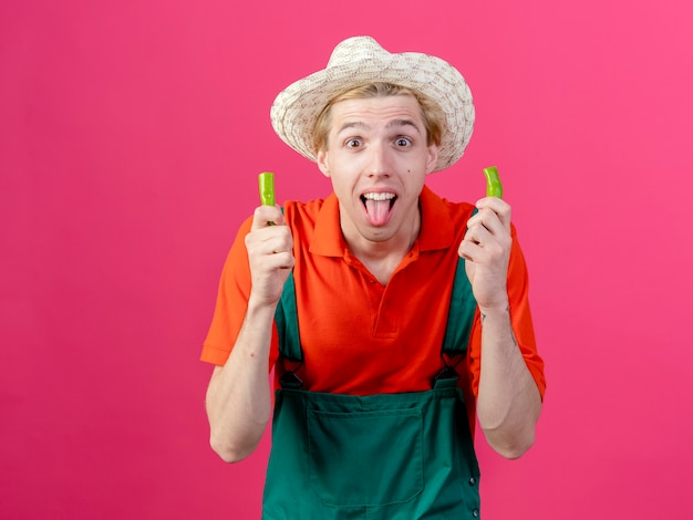 Young gardener man wearing jumpsuit and hat holding halves of green chili pepper