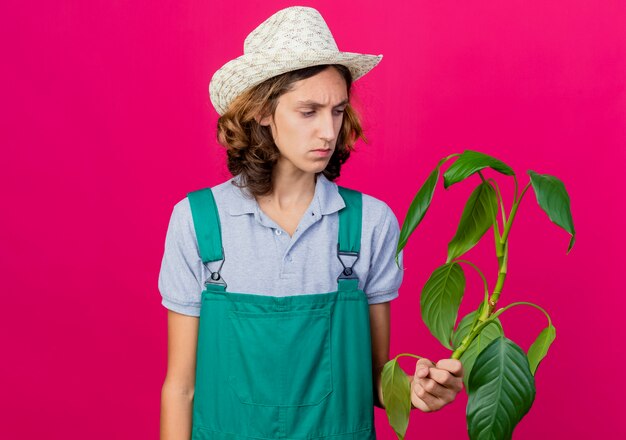 죄수 복과 심각한 얼굴로보고 식물을 들고 모자를 쓰고 젊은 정원사 남자