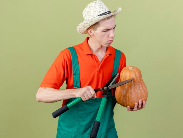 Молодой садовник в комбинезоне и шляпе с тыквой