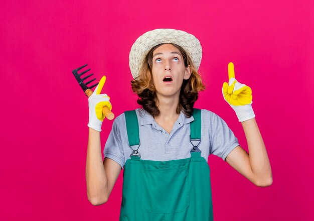 Young gardener man wearing jumpsuit and hat wearing rubber gloves