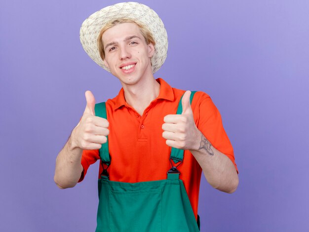 Young gardener man wearing jumpsuit and hat with smile on face