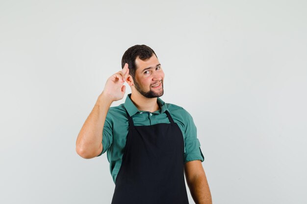 Young gardener showing goodbye gesture in t-shirt,apron and looking grateful , front view.