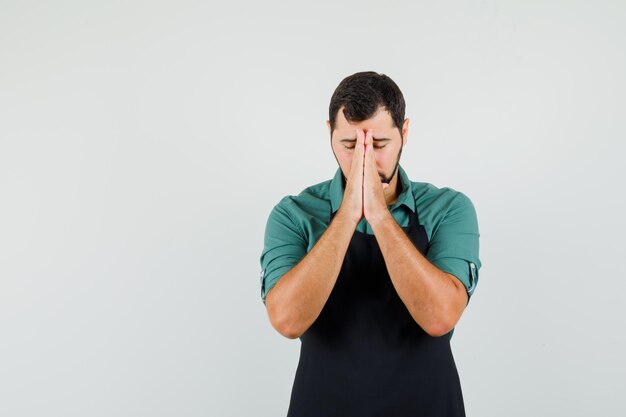 Young gardener showing praying gesture in t-shirt,apron and looking hopeful. front view. space for text