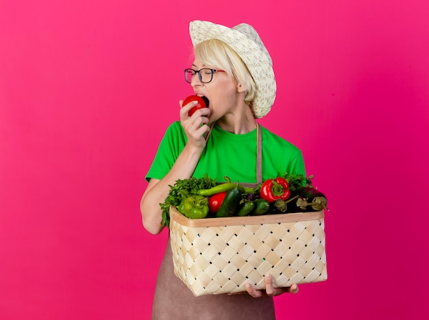 Giovane giardiniere donna con i capelli corti in grembiule e cappello tenendo la cassa piena di verdure