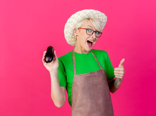 Young gardener woman with short hair in apron and hat holding eggplant