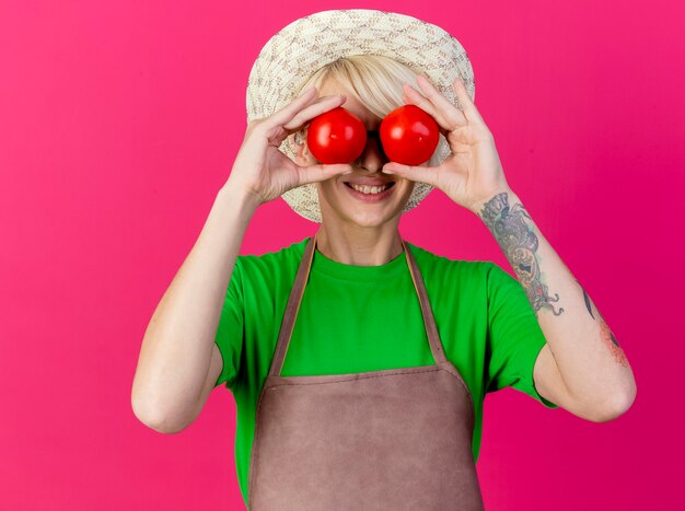 Young gardener woman with short hair in apron and hat holding fresh tomatoes