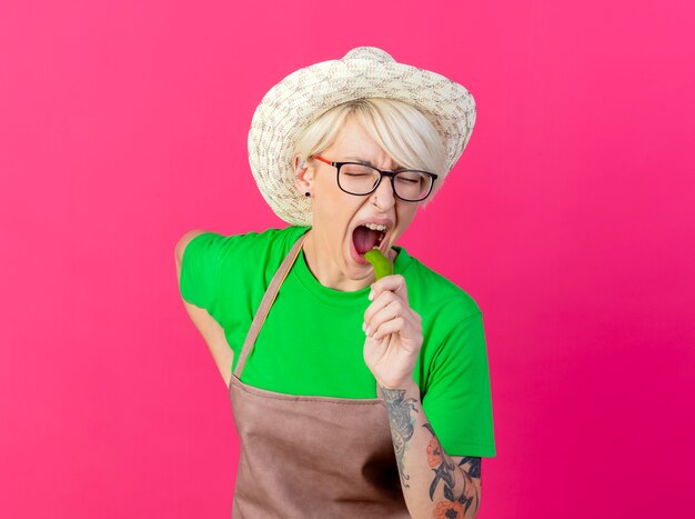 Foto gratuita giovane donna giardiniere con i capelli corti in grembiule e cappello che tiene peperoncino verde