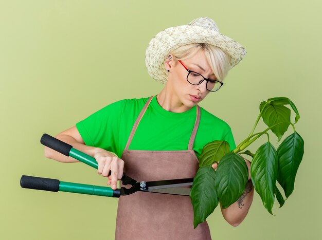 エプロンと帽子保持植物の短い髪の若い庭師の女性