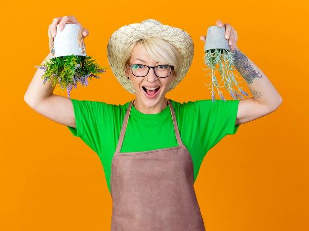 Young gardener woman with short hair in apron and hat holding potted plants