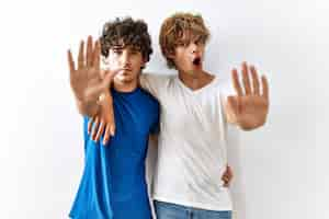 Free photo young gay couple standing together over isolated background doing stop gesture with hands palms angry and frustration expression