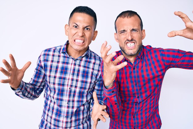 Young gay couple of two men wearing casual clothes shouting frustrated with rage, hands trying to strangle, yelling mad
