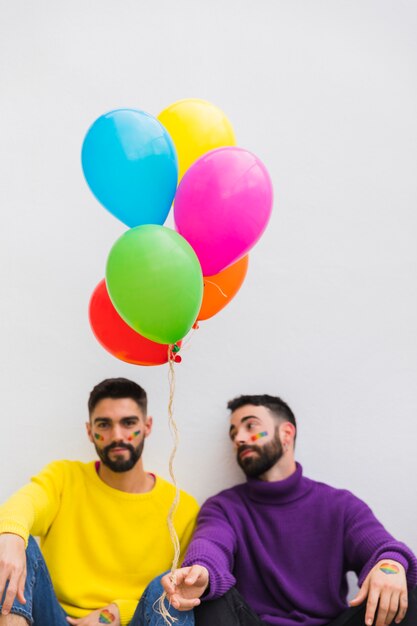Young gays sitting with colorful balloons