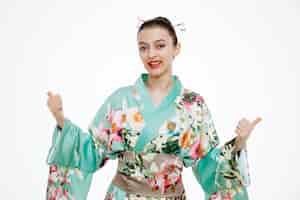 Free photo young geisha woman in traditional japanese kimono looking at front happy and positive showing thumbs up standing over white wall