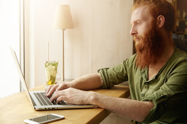 Free photo young ginger man using laptop in cafe