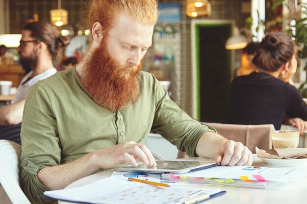 Young ginger man using tablet in cafe