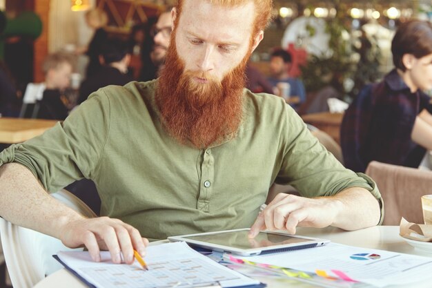 Young ginger man using tablet in cafe