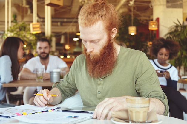 Young ginger man using tablet in cafe