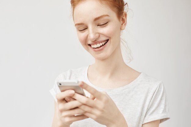Young ginger woman smiling, texting posting photos on social media with a grin