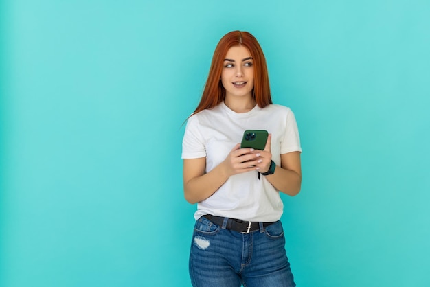 Молодая рыжая женщина пользуется телефоном на бирюзовом фоне