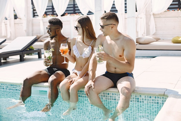 어린 소녀와 두 명의 다인종 남성 친구가 수영장 근처 선베드에서 휴식을 취하고 있습니다.