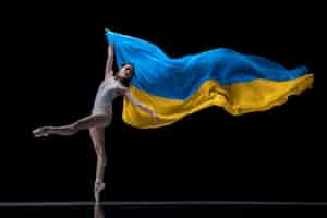 Foto gratuita ballerina di giovane ragazza che balla con un panno dipinto nei colori blu e gialli della bandiera dell'ucraina su sfondo scuro per studio