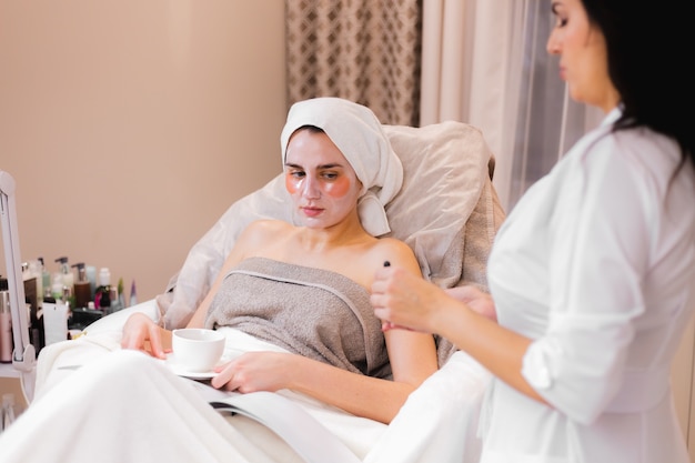 A young girl in a beauty salon in a cosmetology office lies on the bed relaxes with a mask on her face