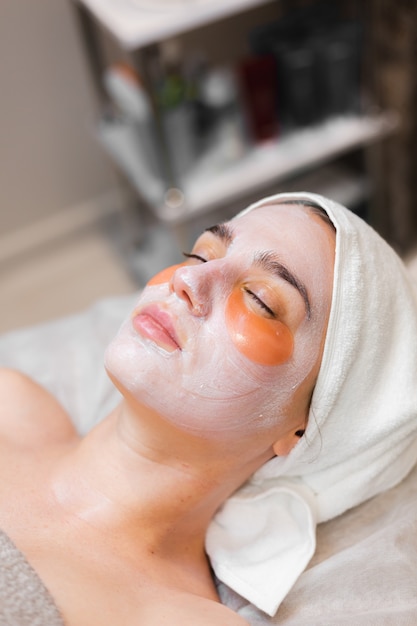 A young girl in a beauty salon in a cosmetology room lies on a bed relaxes with a mask on her face and patches under her eyes