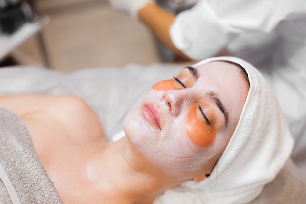 A young girl in a beauty salon in a cosmetology room lies on a bed relaxes with a mask on her face and patches under her eyes