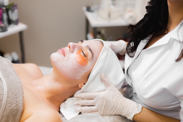 A young girl in a beauty salon in a cosmetology room lies on a bed relaxes with a mask on her face and patches under her eyes