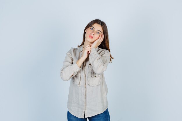 Young girl in beige shirt, jeans leaning cheek on palm and looking attractive , front view.