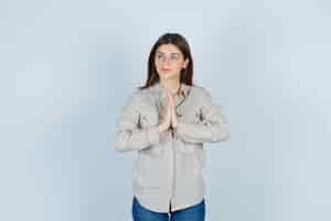 Free photo young girl in beige shirt, jeans showing namaste gesture and looking cute , front view.